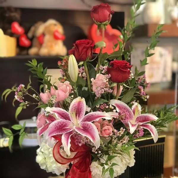Bouquet of red roses and pink lilies in a tall vase with a red ribbon