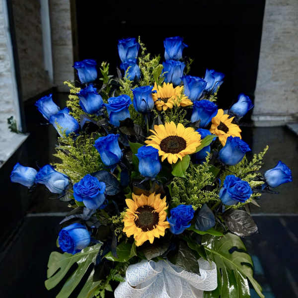 Blue roses and yellow sunflowers in a glass vase with a white ribbon