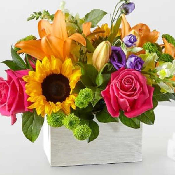 Mixed bouquet in a white square vase with roses, lilies, and a sunflower