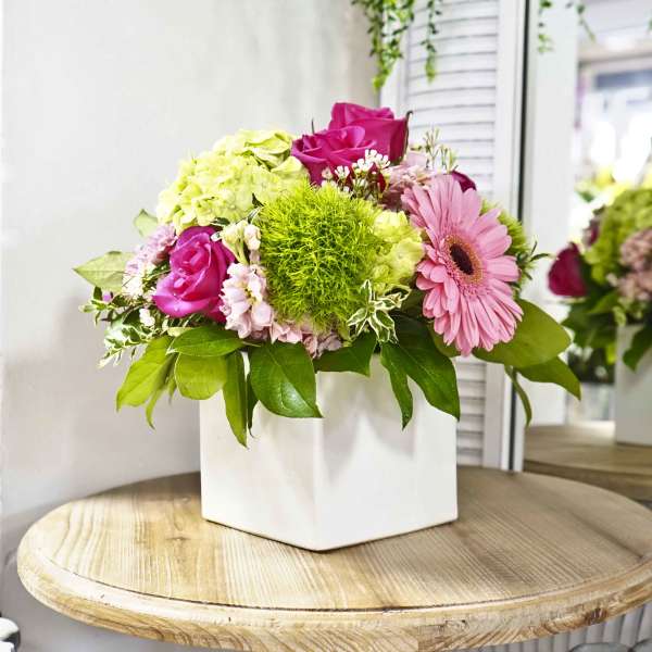 Pink and green floral arrangement in a white square vase