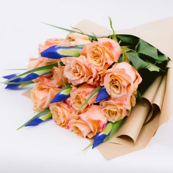Bouquet of peach roses with blue buds wrapped in tan paper