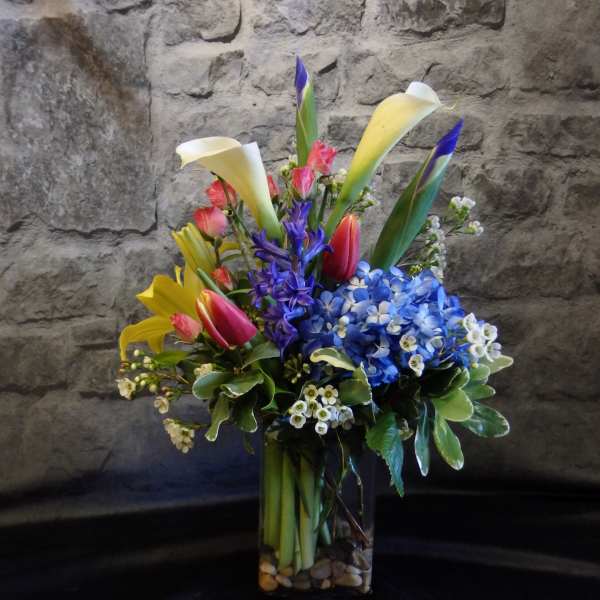 Colorful bouquet with calla lilies, tulips, and blue hydrangeas in a glass vase