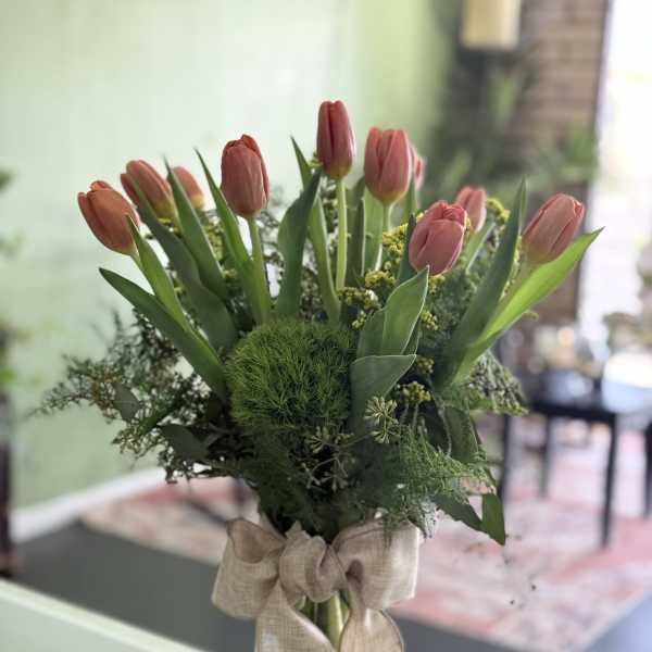 Pink tulips arranged in a clear glass vase with a burlap bow