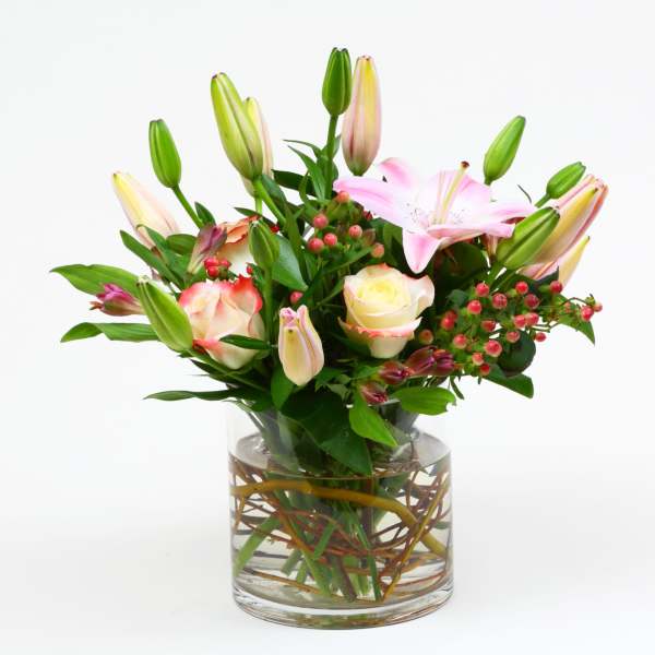 Pink lilies and cream roses with red berries arranged in a clear glass cylinder vase