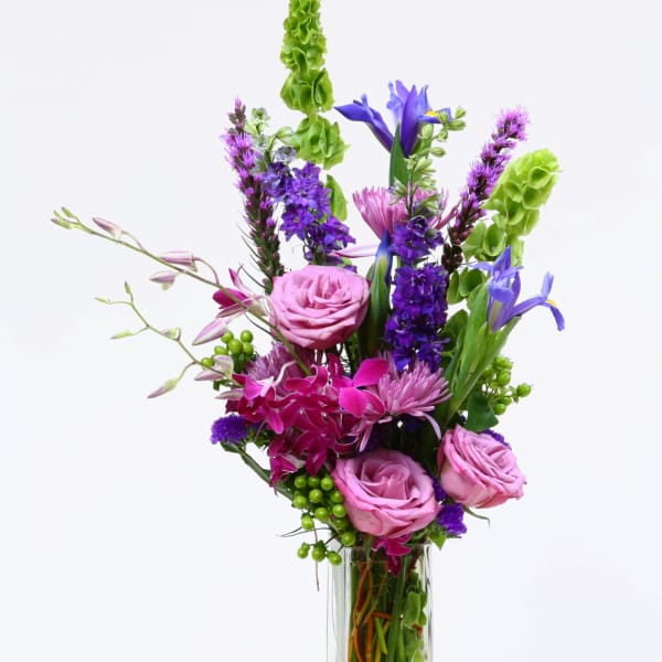 Mixed pink and purple flowers arranged in a tall glass vase
