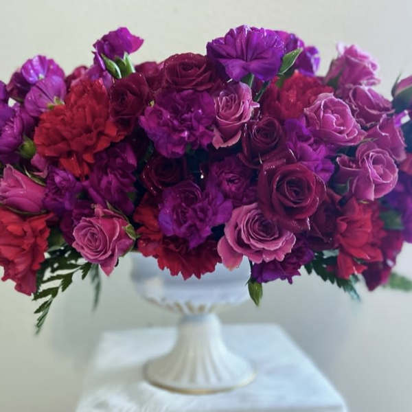 Purple and pink floral arrangement in a white pedestal vase