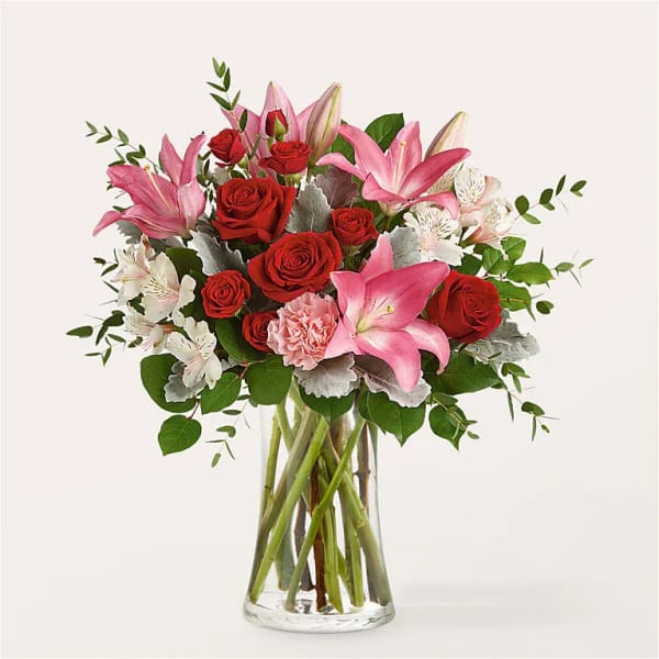 Arrangement of pink lilies, red roses, and white blooms in a clear glass vase.