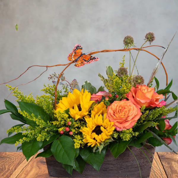 Sunflowers and orange roses in a rectangular wooden container with a butterfly accent