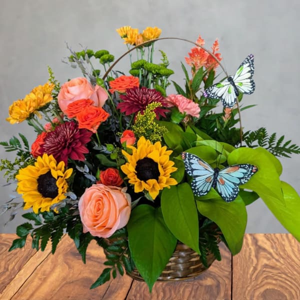 Basket arrangement with sunflowers, roses, mums, and butterfly picks