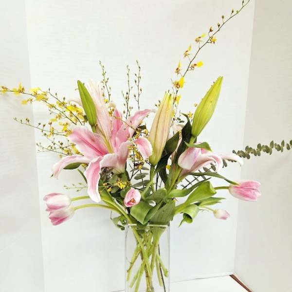 Pink lilies in a tall glass vase with yellow branching accents