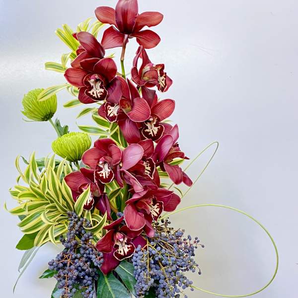 Tall arrangement of red orchids in a dark vase with green accents