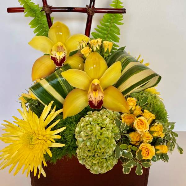 Yellow orchids and chrysanthemums in a brown container with bamboo accents
