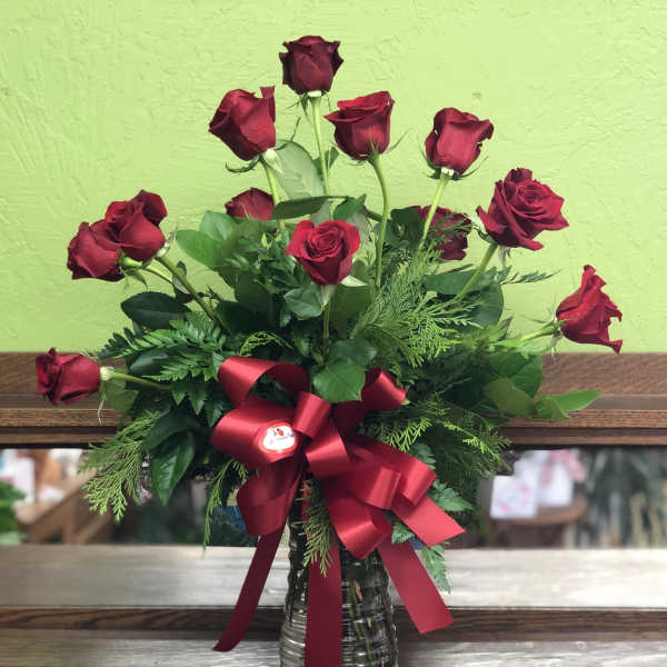 Arrangement of long-stemmed red roses in a clear glass vase with a large red bow.