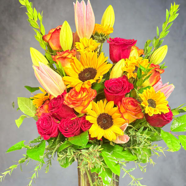 Mixed bouquet of roses, sunflowers, and lilies in a glass vase