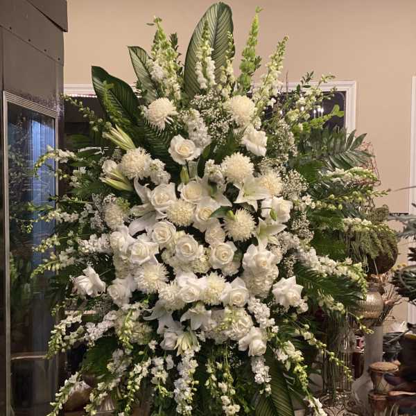 Large white floral standing arrangement with roses, lilies, and cascading blooms