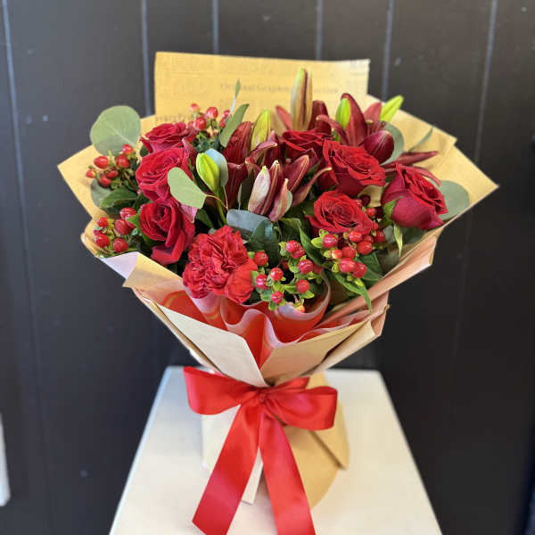 Bouquet of red roses and lilies wrapped in tan paper with a red ribbon