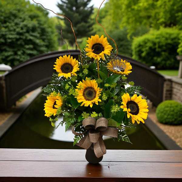 Arrangement of bright yellow sunflowers in a dark vase with a burlap bow and curly branches.