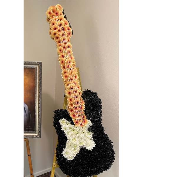 Standing floral arrangement shaped like a guitar with black, peach, and white flowers on an easel.