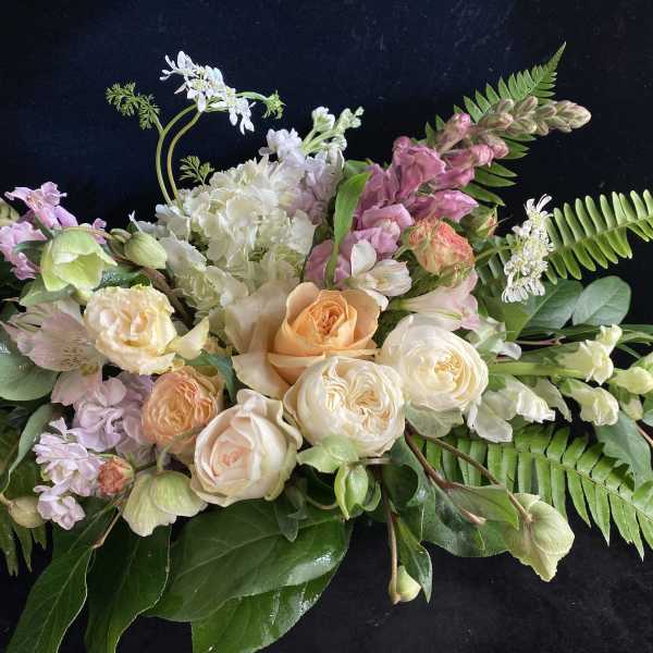 Pastel floral arrangement with roses, hydrangea, and snapdragons on a dark background