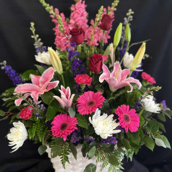 Mixed bouquet in a white basket with pink lilies, roses, and gerbera daisies