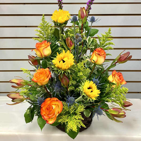 Basket arrangement with orange roses, yellow sunflowers, and purple accents