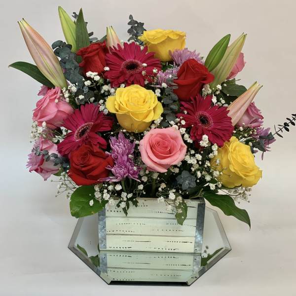 Mixed bouquet of roses, gerbera daisies, and lilies in a mirrored box vase
