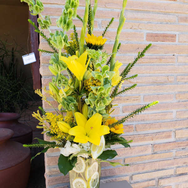 Tall yellow floral arrangement in a glass vase with sliced citrus