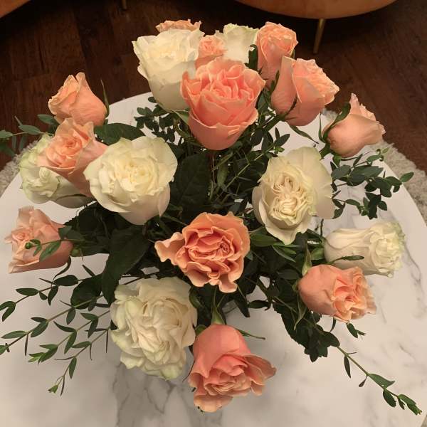 Peach and white roses arranged in a low bouquet on a round table