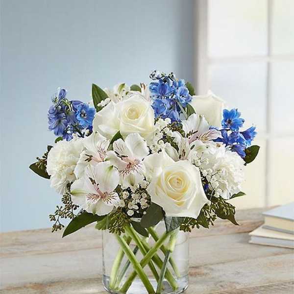 White roses and blue flowers in a clear glass vase