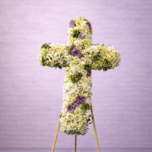 Tall floral cross of white and cream flowers with lavender accents on a wooden easel