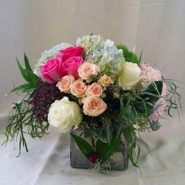 Mixed bouquet of pink, white, and peach roses in a square glass vase