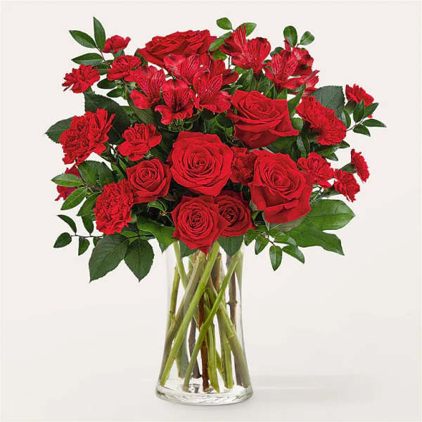 Arrangement of red roses, carnations, and alstroemeria in a clear glass vase