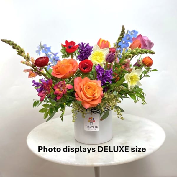 Bright mixed flower arrangement with orange roses, tulips, daffodils and other blooms in a white vase