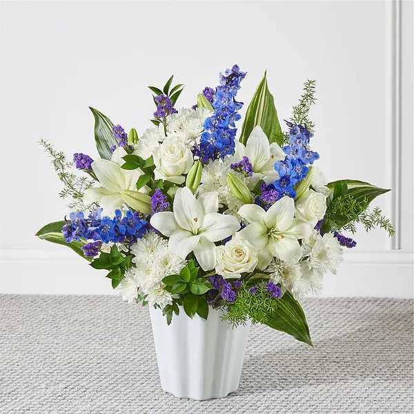 White lilies and roses with blue and purple flowers in a white vase
