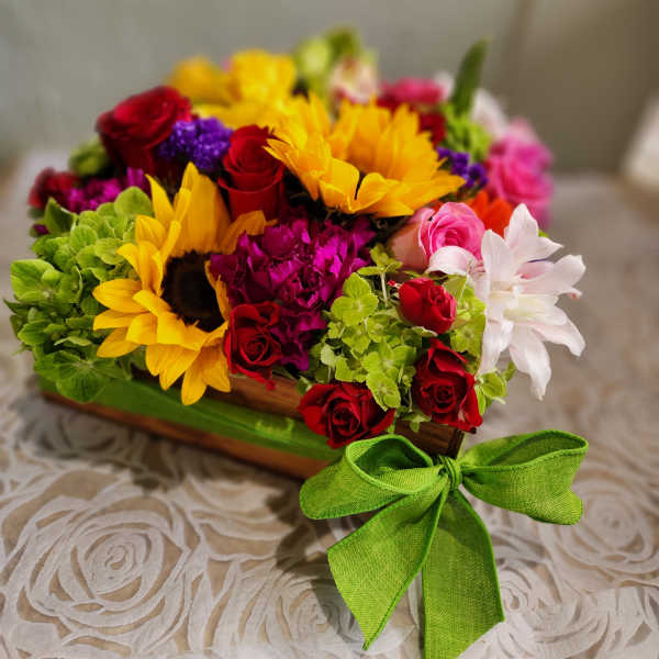 Colorful mixed bouquet with sunflowers, red roses, and pink blooms in a wooden box