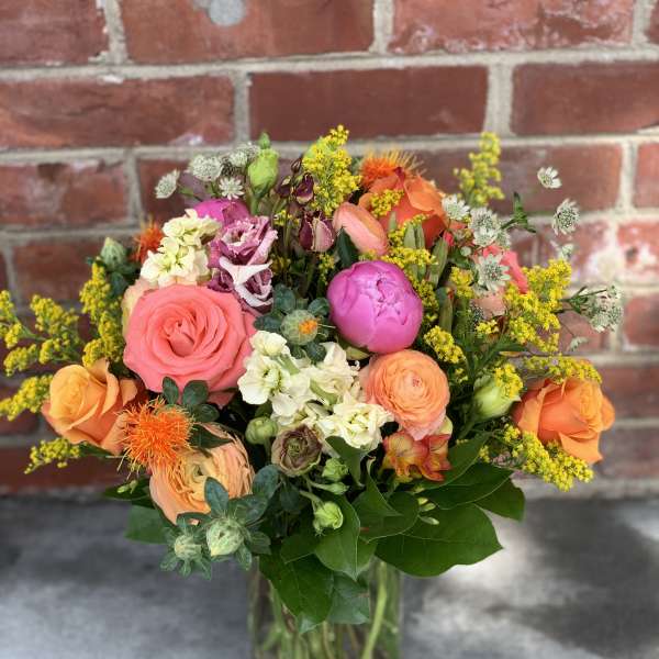 Mixed bouquet of pink, orange, and yellow flowers in a glass vase