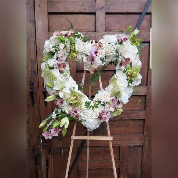Heart-shaped floral wreath of white roses and orchids on an easel