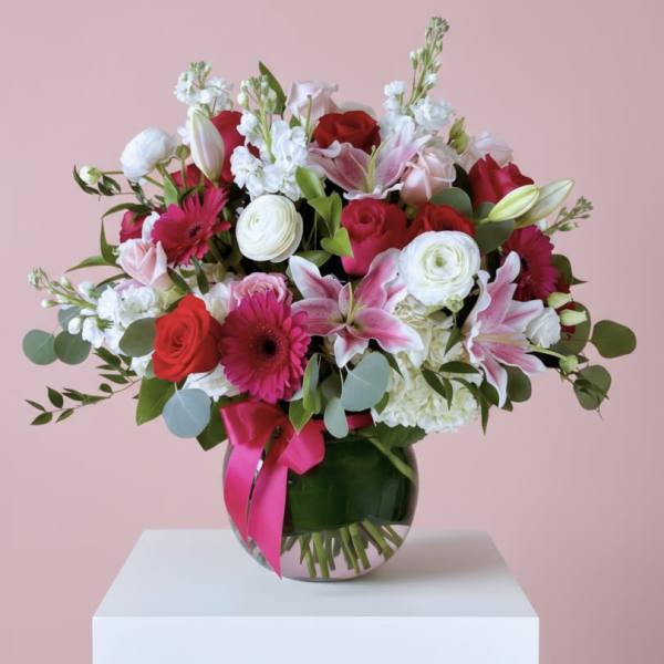 Pink and white mixed bouquet with lilies, roses, and gerberas in a round glass vase with pink bow