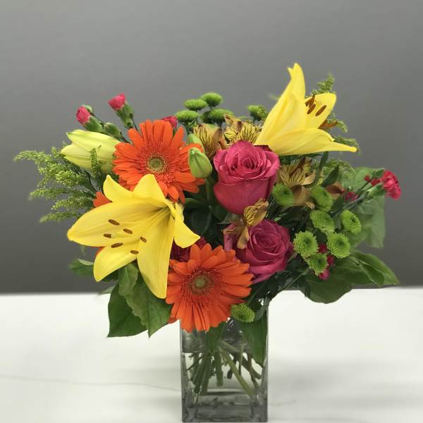 Bouquet of yellow lilies, orange gerberas, and pink roses in a glass vase