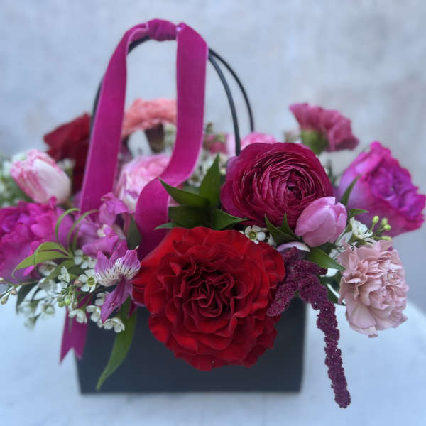 Pink and red mixed flower arrangement in a black handled box with ribbon