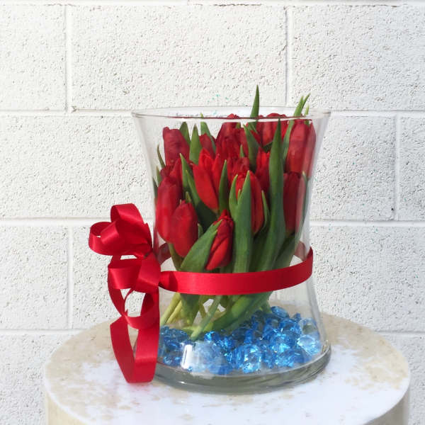 Red tulips in a clear glass vase with a red ribbon and blue stones