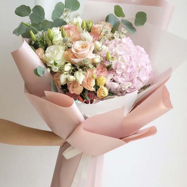 Hand-tied bouquet of pink and cream flowers wrapped in blush paper