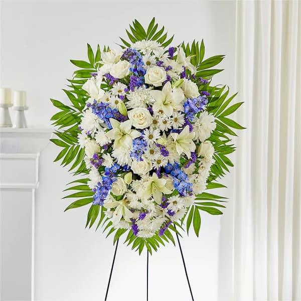 Standing floral spray with white lilies, roses, and purple accents on an easel