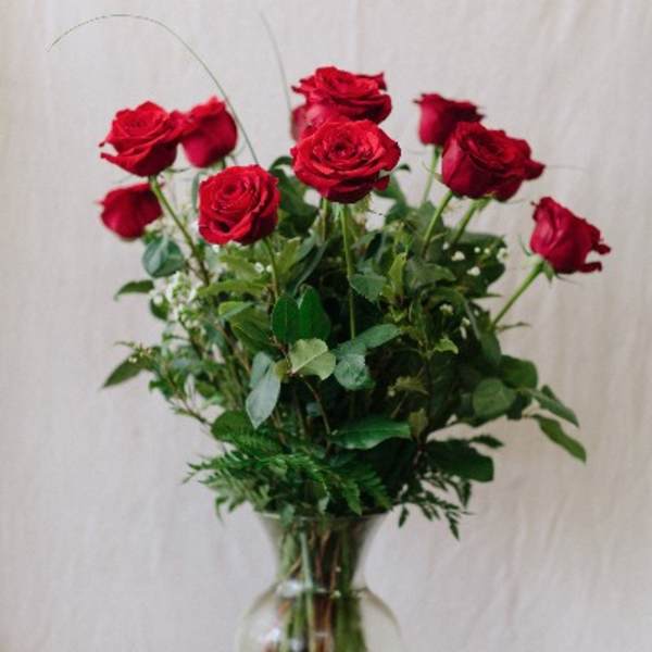 Red roses arranged in a clear glass vase with greenery