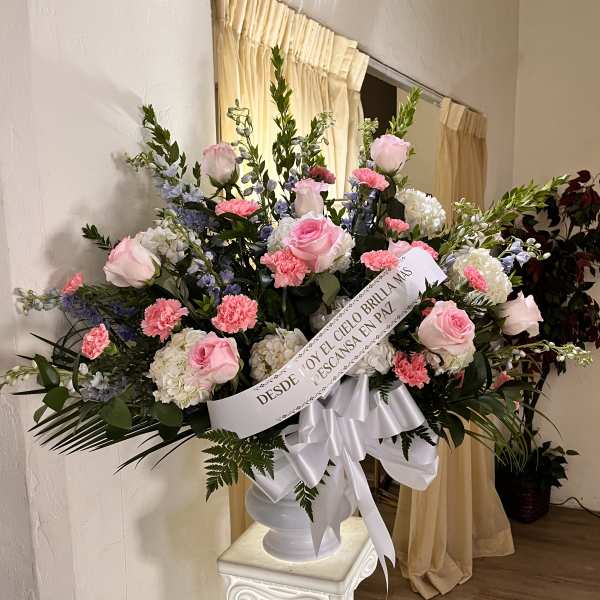 Tall pink and white sympathy arrangement in white urn with memorial ribbon on a pedestal