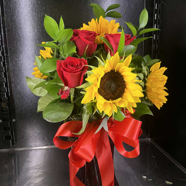 Bouquet of red roses and yellow sunflowers in a black vase with a red ribbon