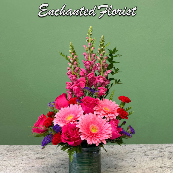 Tall pink floral arrangement with gerbera daisies, roses, and snapdragons in a green glass vase