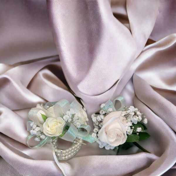 Two white rose corsages with ribbon and pearl accents on satin fabric
