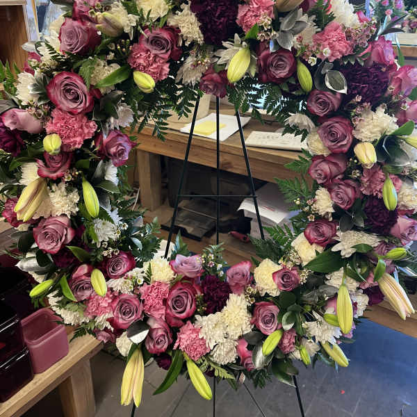 Large floral wreath with pink roses, lilies, and white blooms on a stand