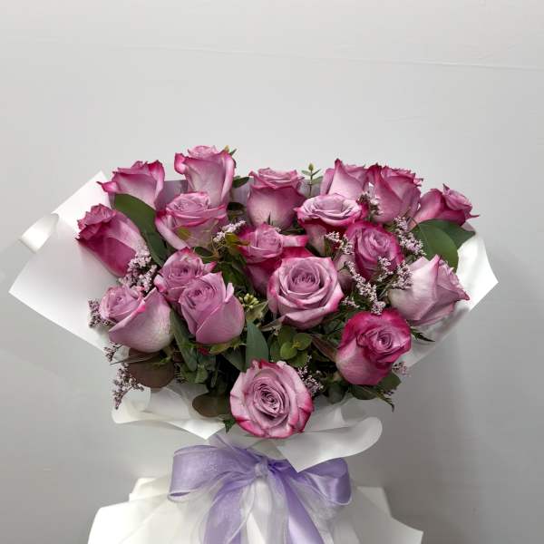 Bouquet of pink roses wrapped in white paper with a lavender ribbon